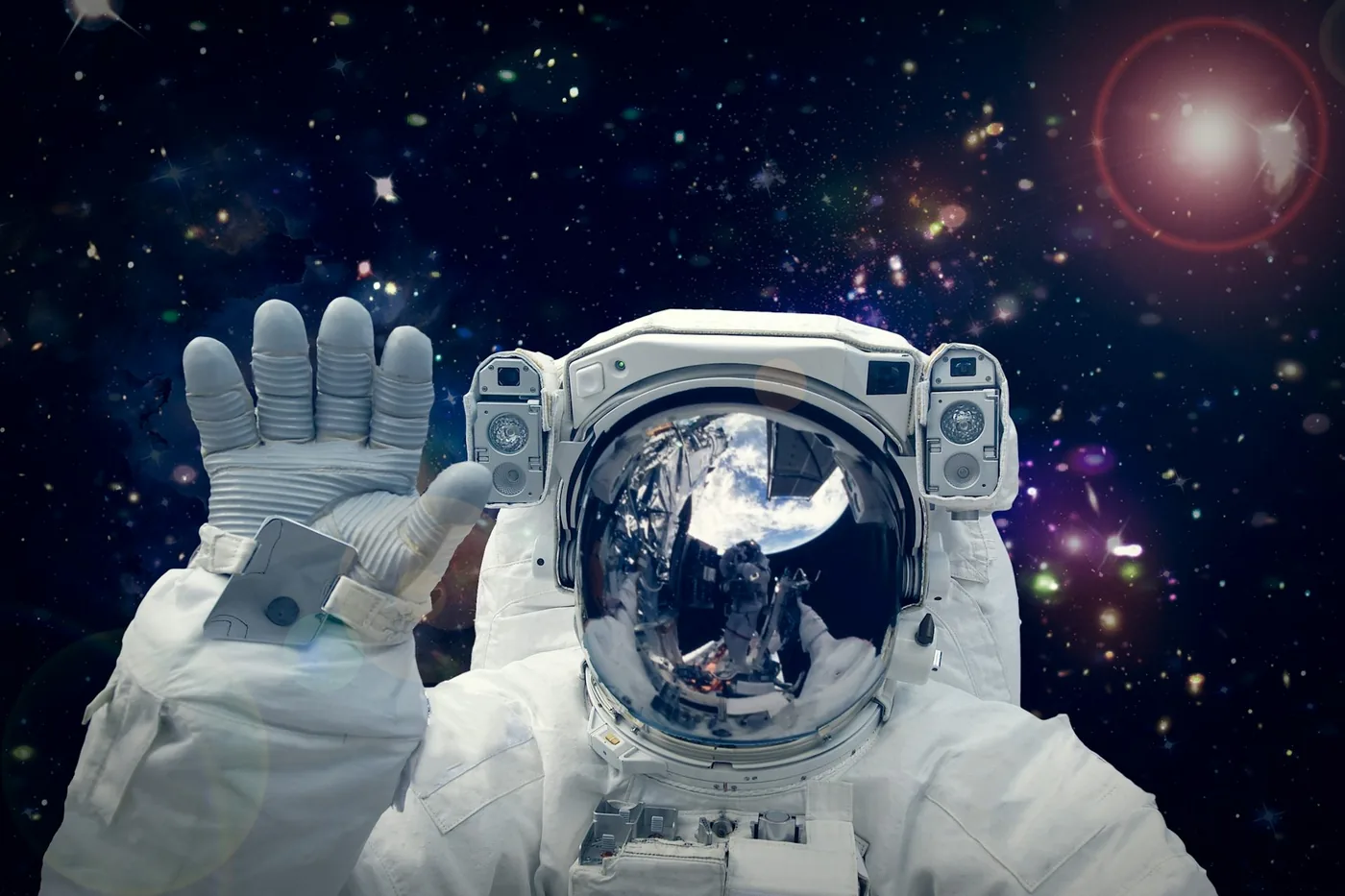 An astronaut in a white spacesuit raises a gloved hand against a star-filled background.