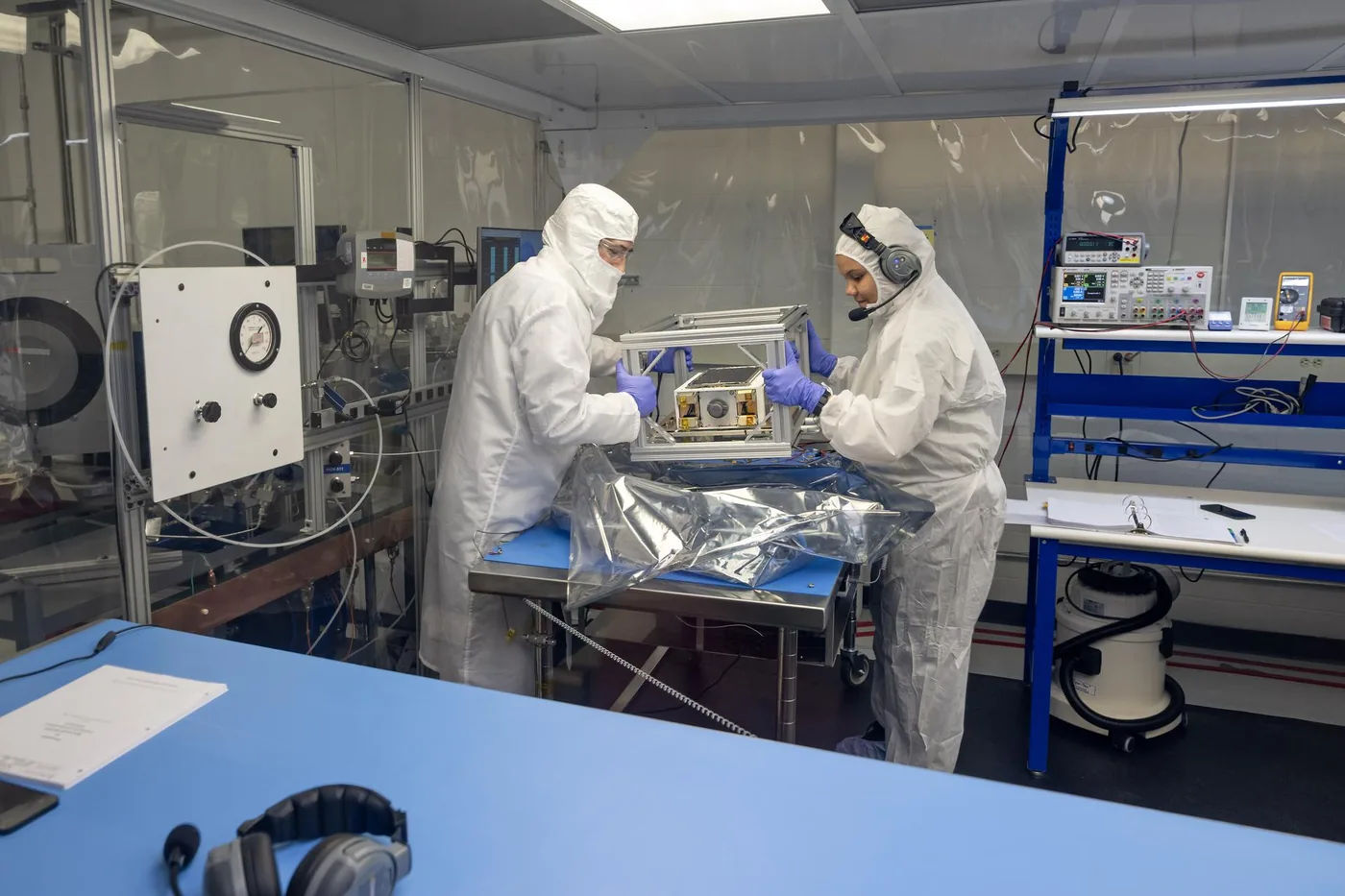 NASA technicians inspecting the dual mode propulsion CubeSat hardware on a laboratory workbench.