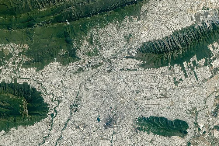 Monterrey mountains form curved, parallel ridges beside the urban area in an astronaut photograph.