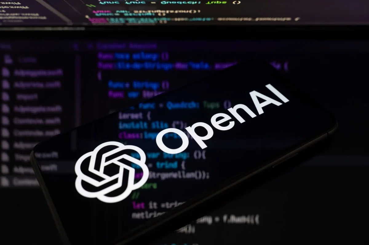 OpenAI logo displayed over programming code featured by TechCrunch reporting on OpenAI agents.