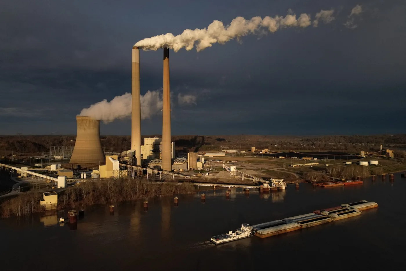 A coal barge navigates the Ohio River past a facility subject to power plant emissions rules.