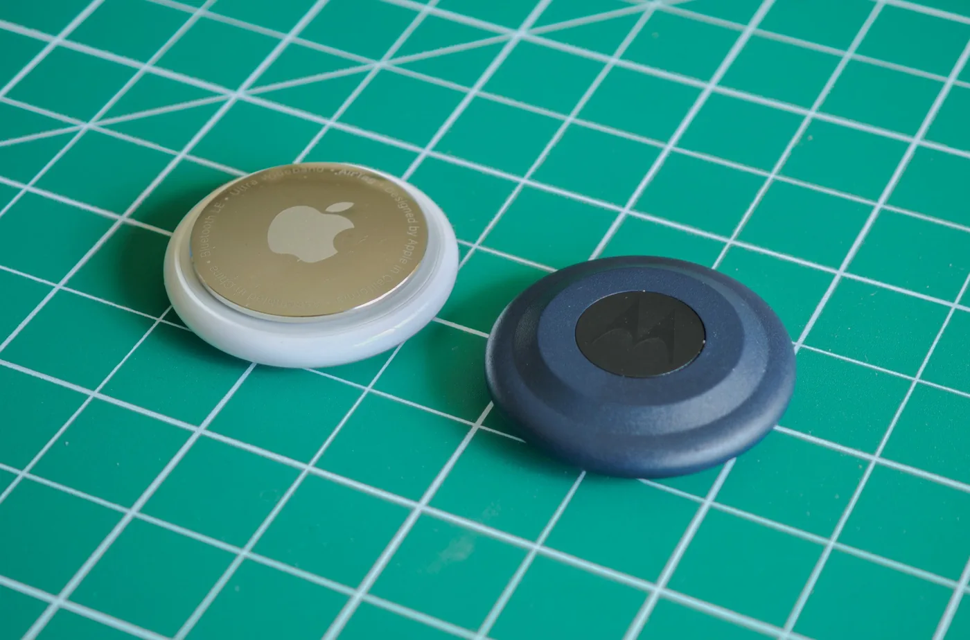 Apple AirTag and Motorola Moto Tag trackers sitting next to each other.