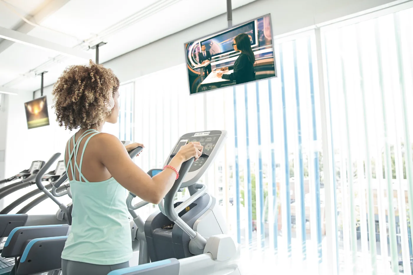 Woman exercising on elliptical in gym near public television screen