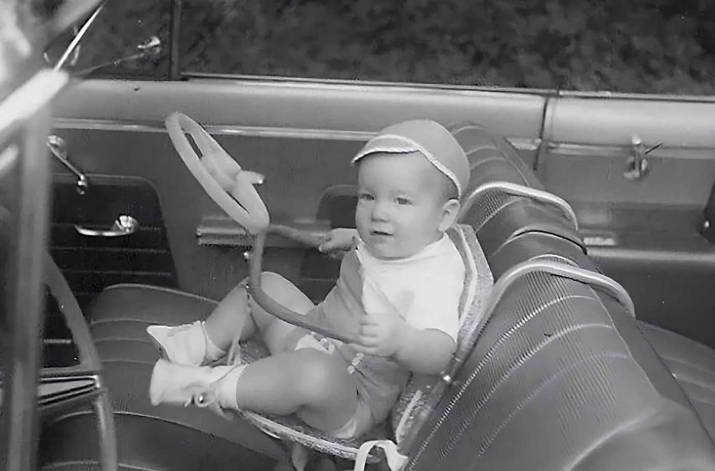 An early elevated baby booster chair installed in the front passenger seat of a vintage automobile.