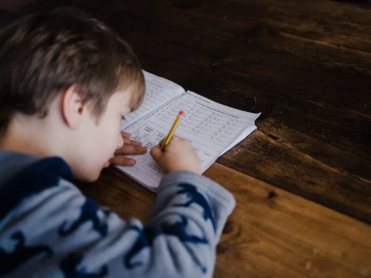 A young boy doing homework at a table, demonstrating focus required for child independent mobility.