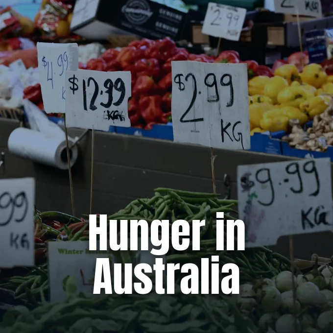 Fresh produce displayed in a grocery market with prominent handwritten price tags showing rising food costs.