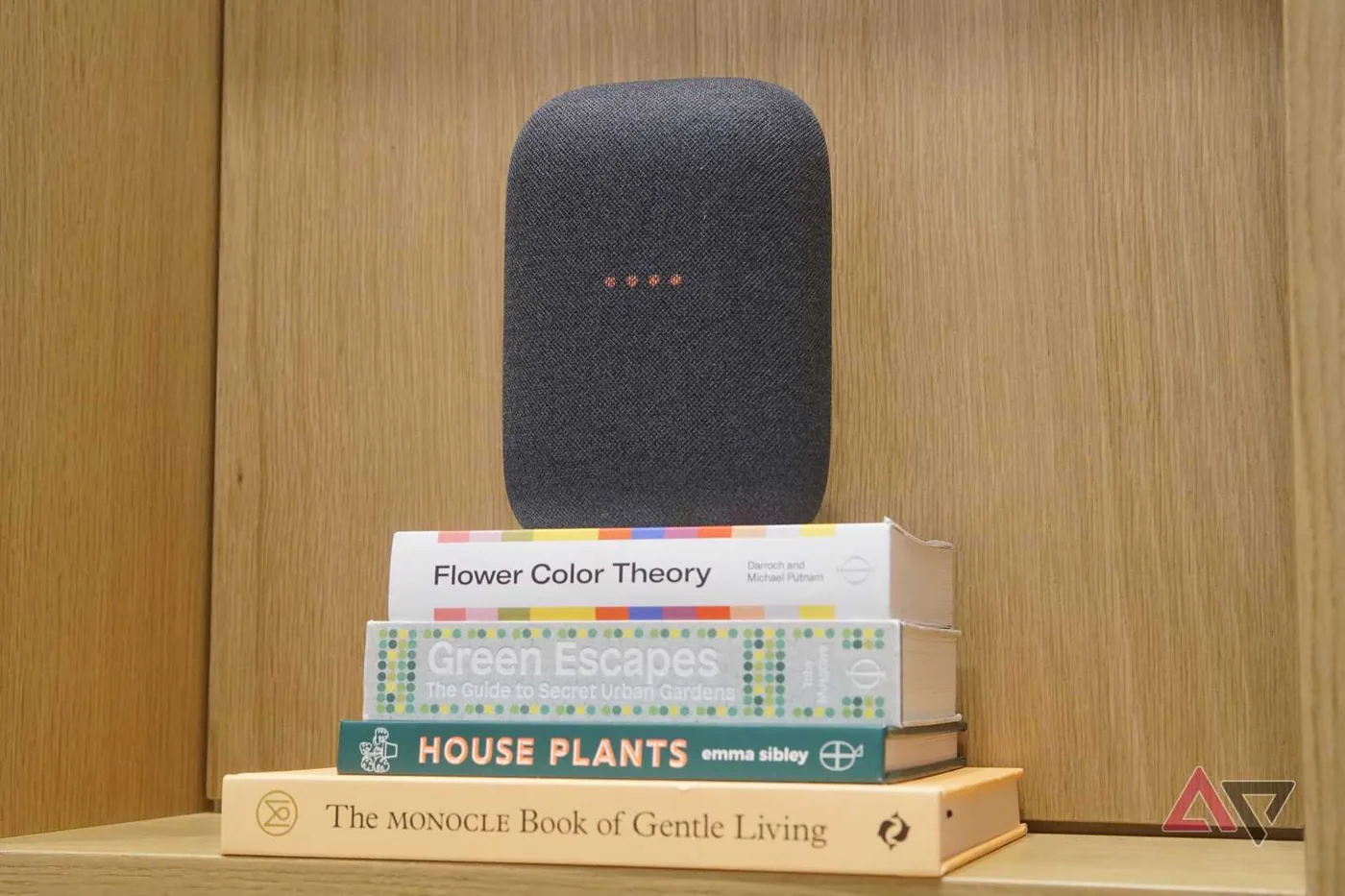 A Google Nest Audio smart speaker in gray sat atop a stack of books.