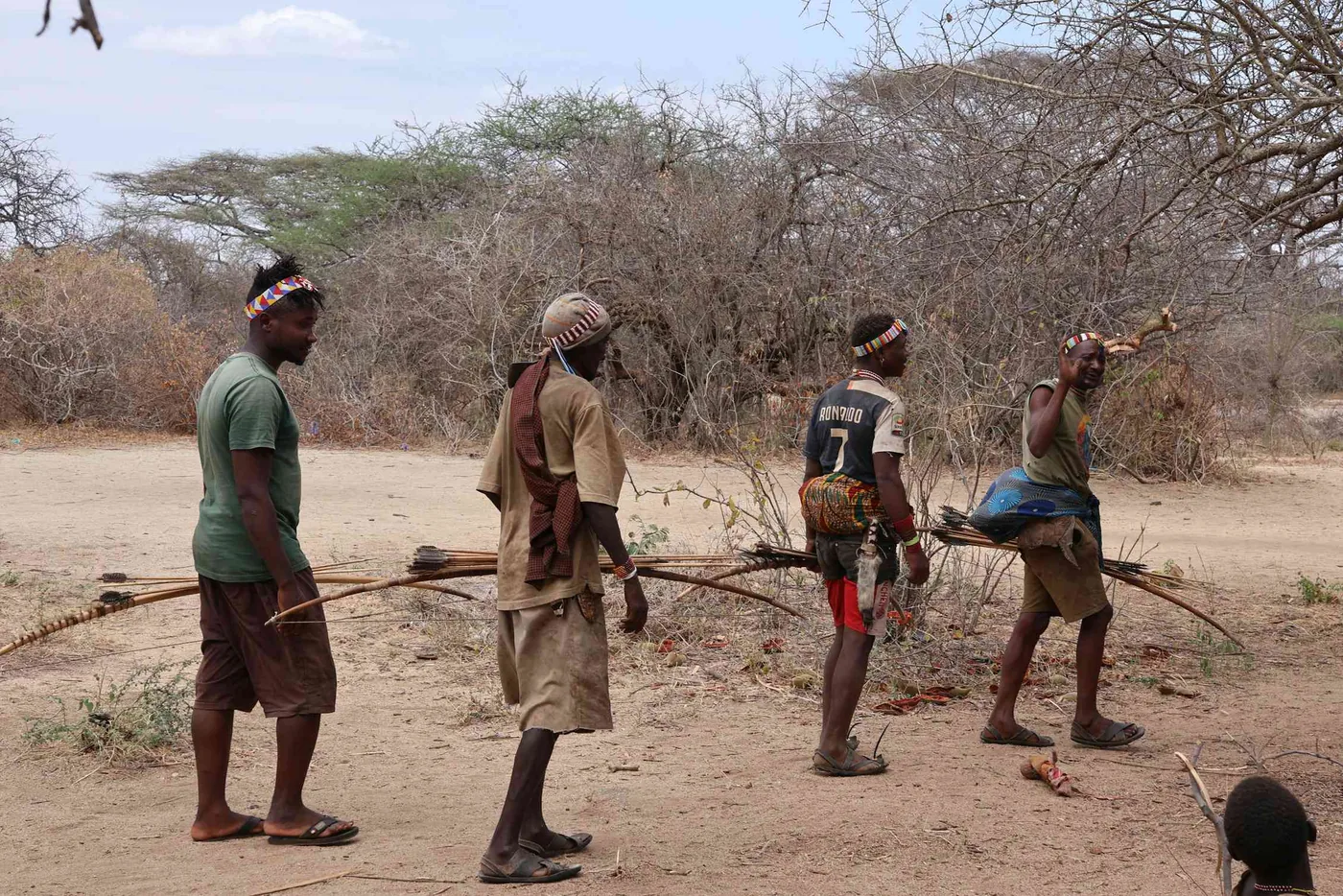 Hadza men carrying hunting bows through dry woodland in northern Tanzania.