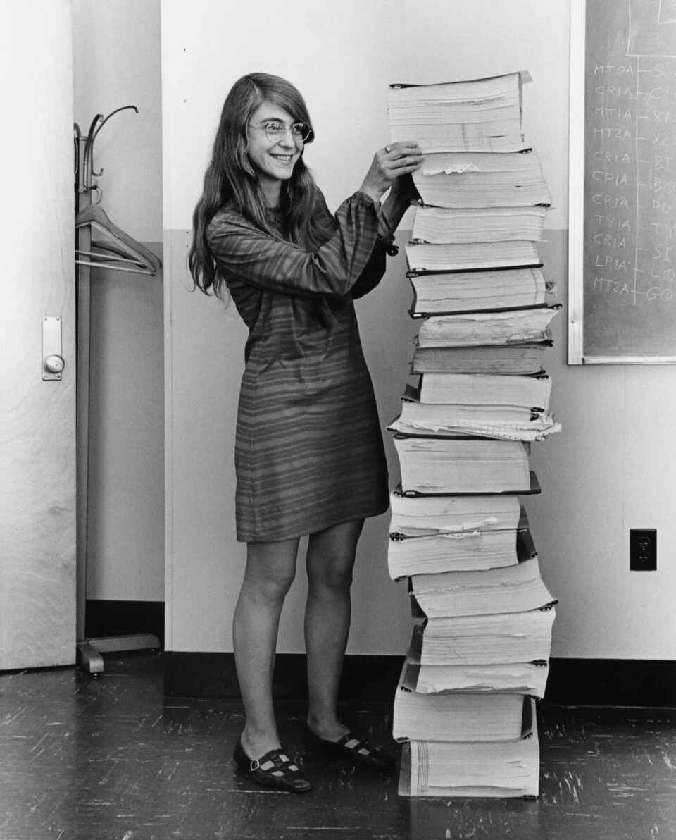 Margaret Hamilton in 1969 standing beside printed listings of Apollo navigation software.