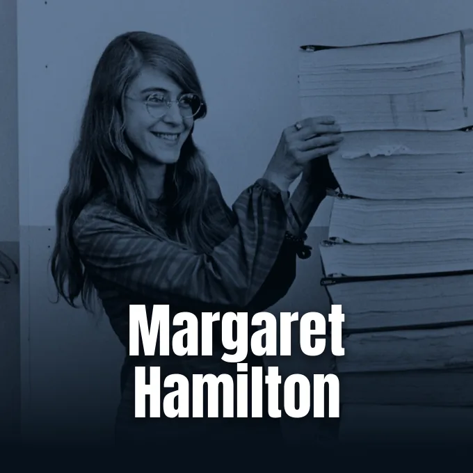 Margaret Hamilton smiling beside a tall stack of printed Apollo guidance computer code listings.