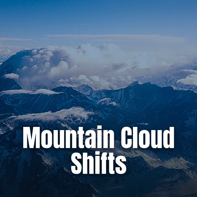 An aerial view of snow-dusted mountain ranges partially covered by rising dense white clouds.