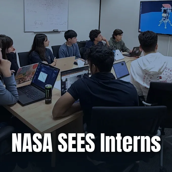 A group of high school interns sitting around a table with laptops viewing a lunar lander model