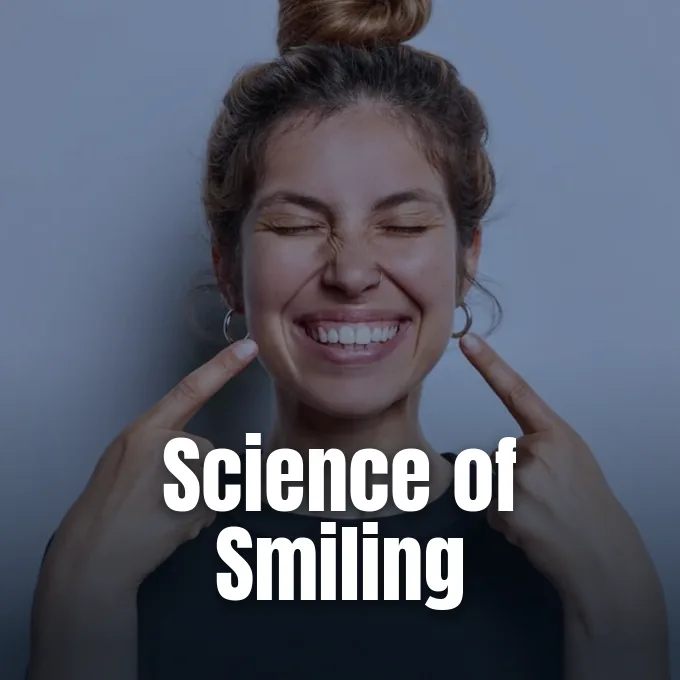 A smiling young woman pointing at her teeth and cheeks against a neutral background.