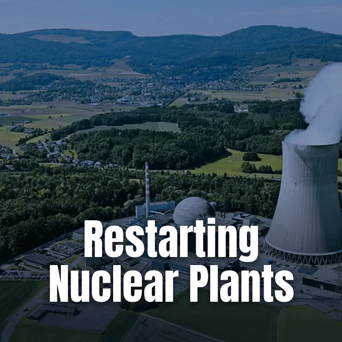 Aerial view of a nuclear power plant facility with a cooling tower emitting steam against hills.