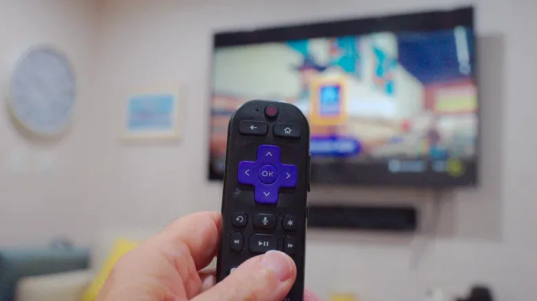 Close-up view of a Roku remote with the Roku star button held in front of a television