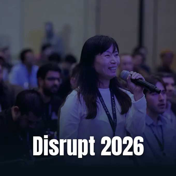 An attendee smiles while speaking into a microphone during an audience session at a conference