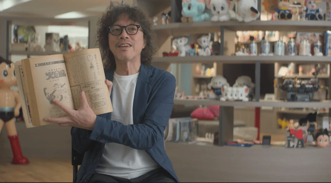 Manga artist Naoki Urasawa holding a book in an interview for the Tezuka God of Manga documentary.