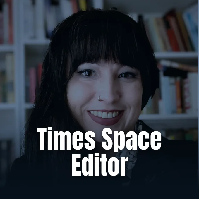 A smiling woman with dark hair and bangs in front of a bookshelf