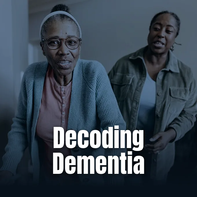 An elderly woman wearing glasses walks indoors accompanied and assisted by a younger woman caregiver.