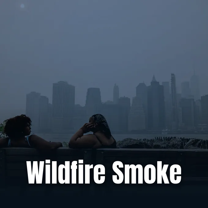 Two people sit on a bench overlooking a city skyline blanketed in dense wildfire haze.